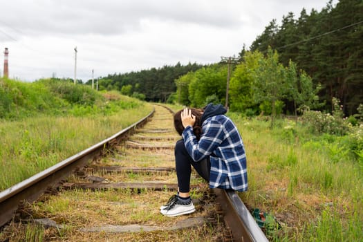 Stress, sadness, loneliness, pain. An upset girl sits on the rails, a psychological situation, help and support