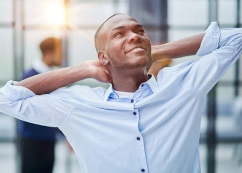 Happy african american young businessman holding hands behind head looking at camera