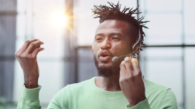 Operator of hot line. Portrait of cheerful african customer service representative with headset in call center, empty space