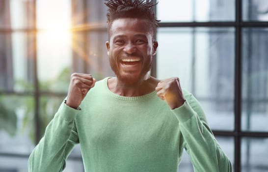 human emotions, reactions and feelings. Joyful young black man clenching his fists expressing joy and success,