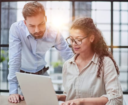 Colleagues check documents using a laptop. A man and a woman are sitting together looking at a laptop. business concept