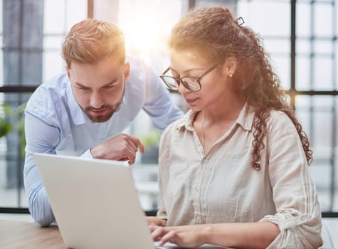 Colleagues check documents using a laptop. A man and a woman are sitting together looking at a laptop. business concept