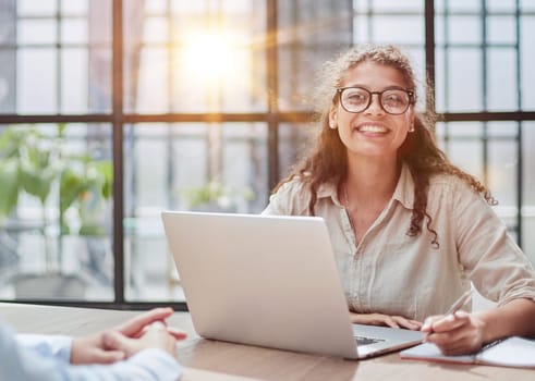 manager in glasses sitting at the table receives a client in the office looking at the camera