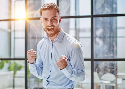 Portrait of a young businessman in a blue shirt shaking his fists celebrating his success in the office