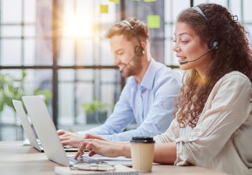 male call-center operator with headphones sitting at modern office, consulting online information in a laptop, looking up information in a file in order to be of assistance to the client.