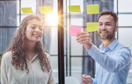 Creative professionals standing and discussing in office behind glass wall with sticky notes