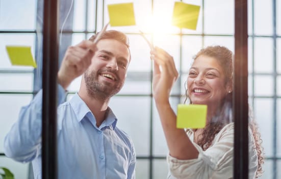 Creative professionals standing and discussing in office behind glass wall with sticky notes