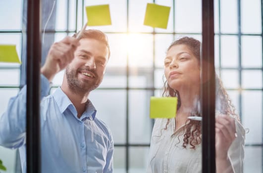 Creative professionals standing and discussing in office behind glass wall with sticky notes