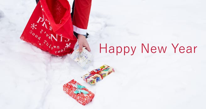 A man dressed as Santa Claus collects gifts in a snowy forest in the snow, colorful boxes with gifts. Happy New Year lettering
