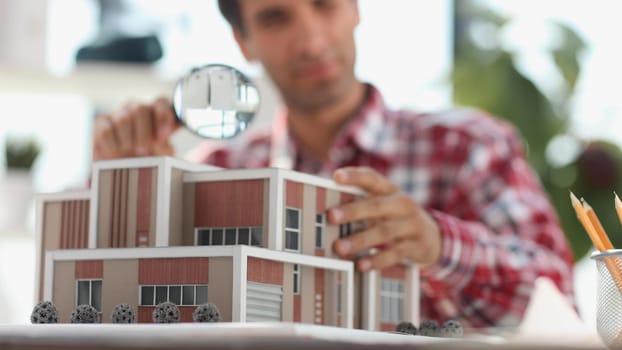 male appraiser looking at house model through magnifying glass.