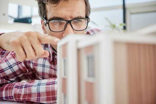 Young Male Designer Assembling Wooden Pieces into a House Miniature on Top of the Table with Blueprint.