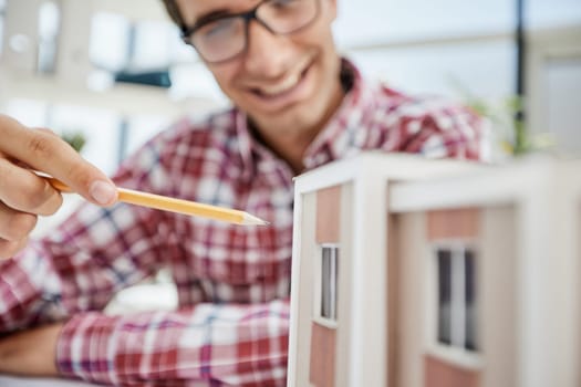Young Male Designer Assembling Wooden Pieces into a House Miniature on Top of the Table with Blueprint.