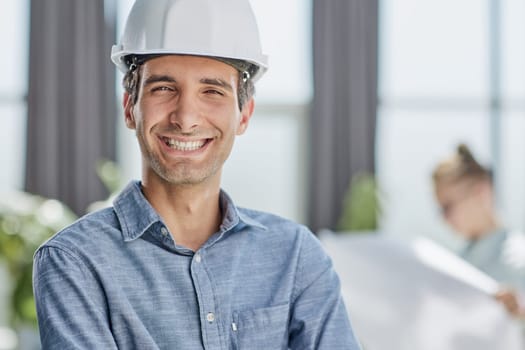 Smiling young unshaven business man in light shirt protective construction helmet.