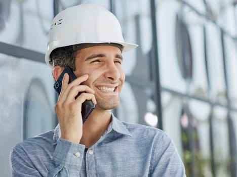 smiling architect in a hard hat speaks on a smartphone.