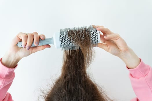 Hair close-up, comb in hand. The girl dries her hair with a comb. The concept of home care, drying healthy hair with a hairdryer and brush