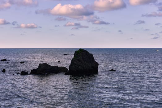 Big rocks in the ocean at low tide. Calm sea, black stones, cliffs, fontal view, sky with clouds