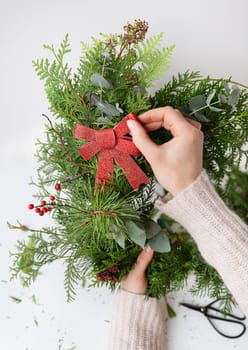 Stylish Christmas wreath for the interior, hang the wreath on the door. Handmade, the girl is holding a freshly made wreath with a beautiful red bow. Festive atmosphere