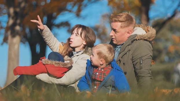 A family and their children enjoy the golden fall in the park sitting on the leaves