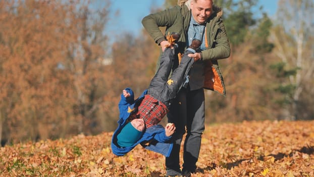 A father spins his son by his feet in the park in the fall