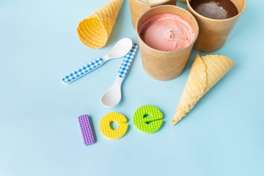 Ice cream in a box with different flavors - strawberry, chocolate, vanilla stands on a blue background along with a waffle cone and a spoon. Ice inscription