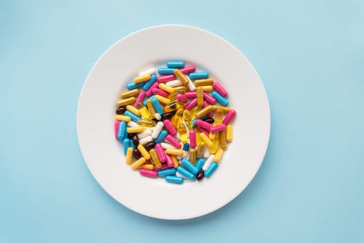 Colorful pills in a large white bowl on a blue background. The concept of health and evidence-based medicine. Place for an inscription