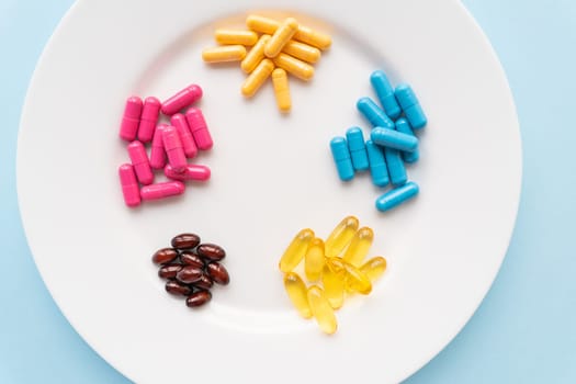Food supplements of bright color lie on a white plate on a blue background. Concept of health support and lack of vitamins