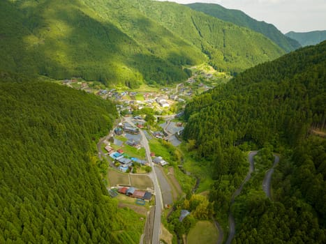 Aerial view of dappled sun on remote village in green forested mountains of Japan. High quality photo