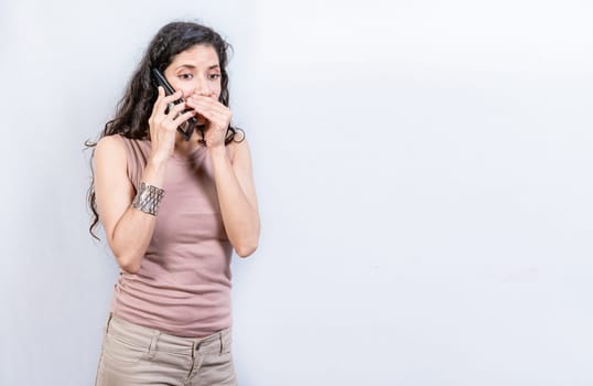 Mysterious young woman talking on the phone isolated. Woman talking secretly on the phone isolated. Latin woman talking on the phone quietly isolated.