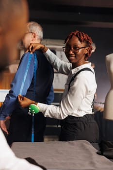 Experienced seamstress providing arm measurements to suitmaking tailor in sartorial process. Skilled precise needleworker using tape to assess proper bespoken suit sleave length