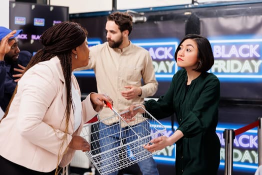Black Friday chaos. People shoppers behaving rude and aggressive while shopping during sales, fight between bargain-hunters. Two angry emotional women fighting over shopping basket