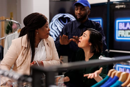 Two diverse women fighting over discount items during Black Friday shopping. Security guard dealing with crazy bargain hunters in clothing store, people going crazy with seasonal sales