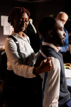 Tailor assistant doing bespoken sartorial fit measuring under expert suitmaker guidance. Aspiring seamstress apprentice learning craftmanship from seasoned senior master in atelier shop workspace