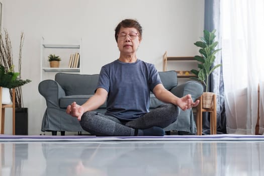 A senior woman finds inner peace through yoga and meditation at home, embracing relaxation and tranquility of the mind. Calm barefoot middle aged female sitting on carpet in half lotus posture, making mudra gesture and closing eyes, having peaceful facial expression, doing mindful meditation, concentrating on breathing.