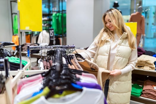 Happy young woman buying new clothes in store. Sale shopping fashion and people concept.