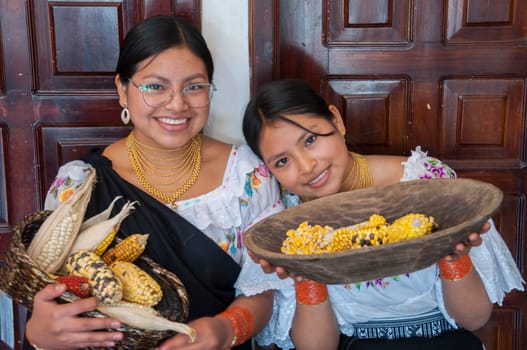 two smiling indigenous people from otavalo in traditional dress showing a basket with the harvest of ears of corn. High quality photo