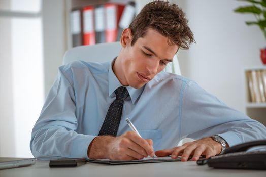 Executive male working at desk looking at documents and accounts. He is holding a pen and looking concentrated and serious.