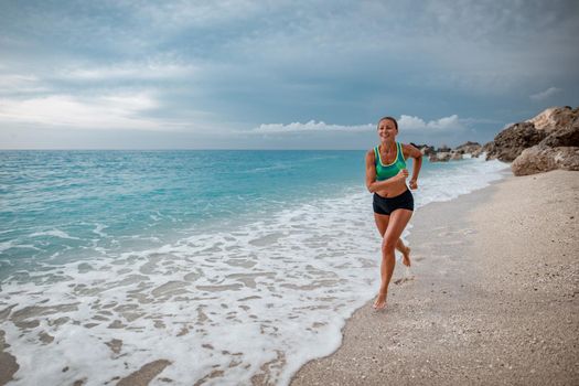 Beautiful young woman is running along the sea shore in the end of the day.