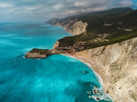 Aerial views of the turquoise sea water with wild seashore and waves reaching sandy beach and steeply rocks on a sunny day. View on the Porto Katsiki beach on the west coast of the island of Lefkada, Greece.