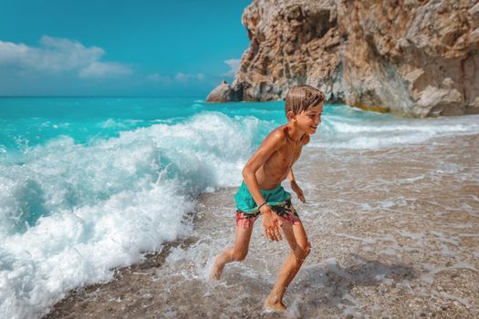 Cute boy enjoying on the beach running from the sea waves. 
