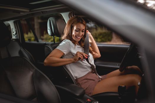 Young smiling happy attractive woman is pulling on seat belt inside car.