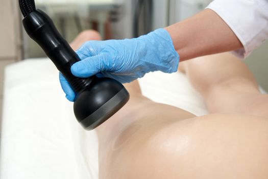 professional cosmetologist using ultrasound cavitation machine on a female client. woman getting contouring anti-cellulite body treatment at beauty salon