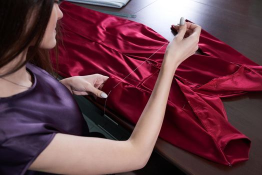 Beautiful young dressmaker in workroom sewing red dress