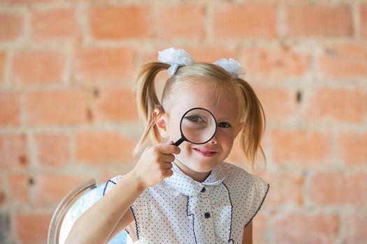 Cute little girl in school uniform with magnifier if front of her eye, back to school concept