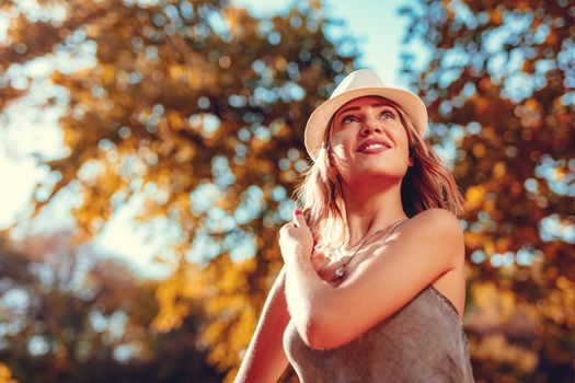 Portrait of a beautiful smiling young woman in the nature in early autumn sunny day. Looking away.