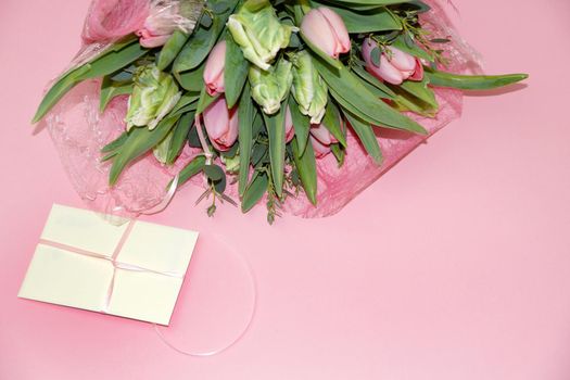 a bouquet of tulips and a gift envelope on a pink background, copy space