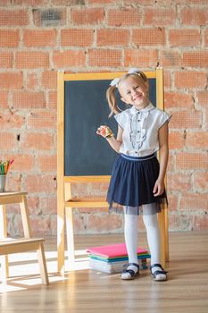 Adorable caucasian private school kindergarten girl smiling in front of blackboard with a bell in her hands, back to school concept