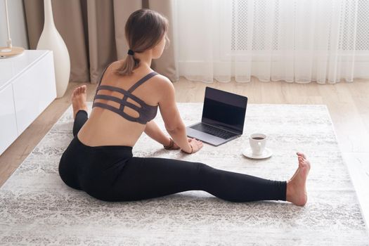 A sporty woman in sportswear is sitting on the floor using a laptop at home in the living room. Sport and recreation concept.
