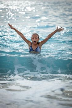 A little girl having fun in the waves of the sea and the drops of water are splashing all over her.
