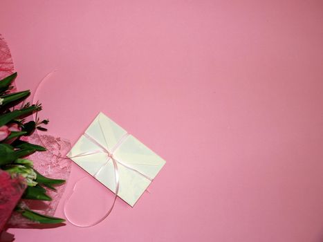 a bouquet of tulips and a gift envelope on a pink background, copy space