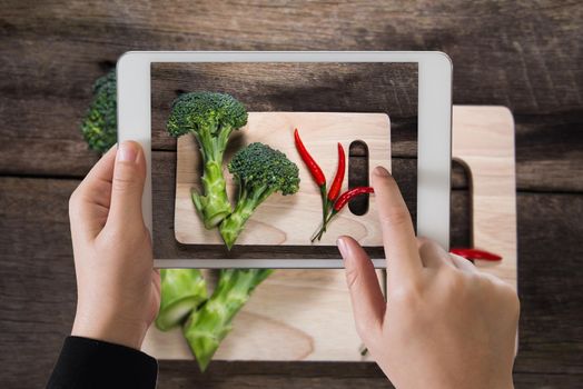 ipad take photo of fresh broccoli and chilli on wood table background. top view